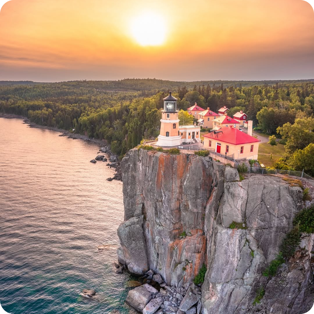Photo from above of Split Rock Lighthouse and State park on the edge of a cliff with a sunset in the background